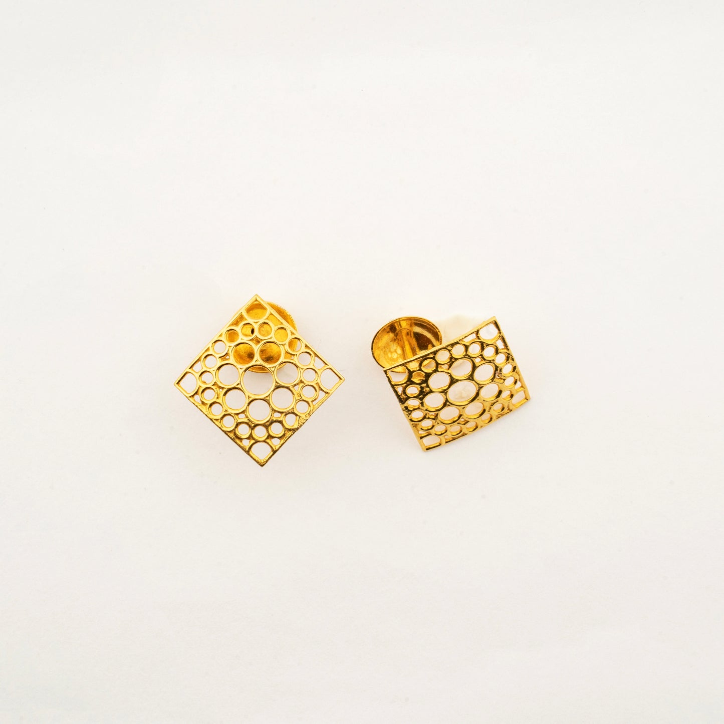 Close-up of Sculptyx Oculus Aurea 18K gold geometric stud earrings showcasing detailed openwork craftsmanship.